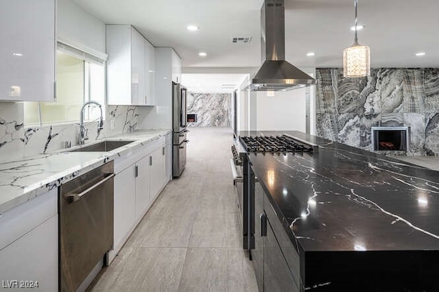 kitchen featuring light stone counters, stainless steel appliances, sink, wall chimney range hood, and white cabinets