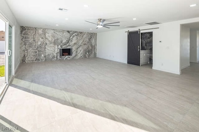 unfurnished living room with a barn door, ceiling fan, and a high end fireplace