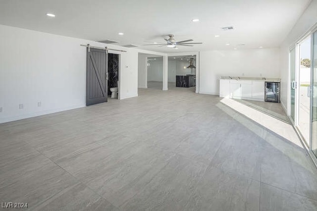 unfurnished living room featuring ceiling fan, a barn door, and beverage cooler