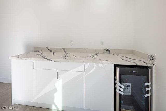 kitchen with light stone countertops, white cabinetry, light wood-type flooring, and beverage cooler