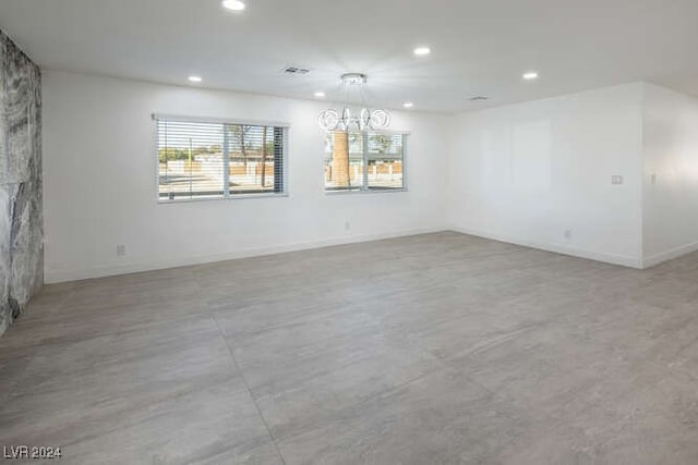 unfurnished room with a stone fireplace and a chandelier