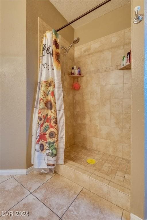 bathroom with tile patterned flooring, tiled shower, a textured ceiling, and baseboards