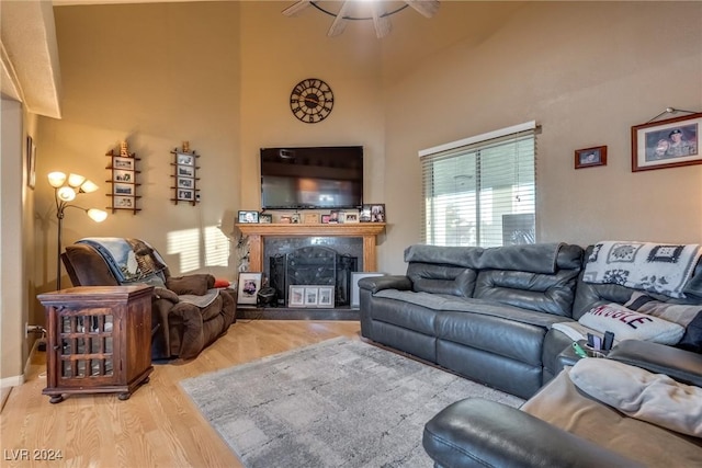 living room featuring light wood-type flooring, a premium fireplace, a high ceiling, and a ceiling fan