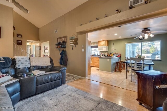 living area with light wood finished floors, visible vents, baseboards, ceiling fan, and high vaulted ceiling