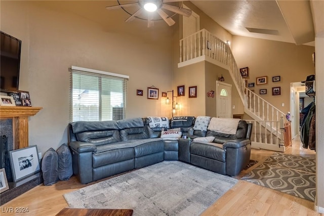 living area featuring a ceiling fan, wood finished floors, a towering ceiling, and stairs