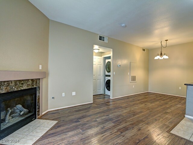 unfurnished living room featuring a tile fireplace, hardwood / wood-style floors, an inviting chandelier, and stacked washer / dryer