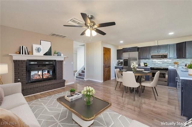 living room featuring ceiling fan, a fireplace, and light wood-type flooring