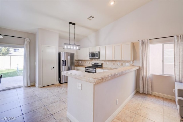 kitchen featuring kitchen peninsula, decorative light fixtures, decorative backsplash, light tile patterned floors, and appliances with stainless steel finishes