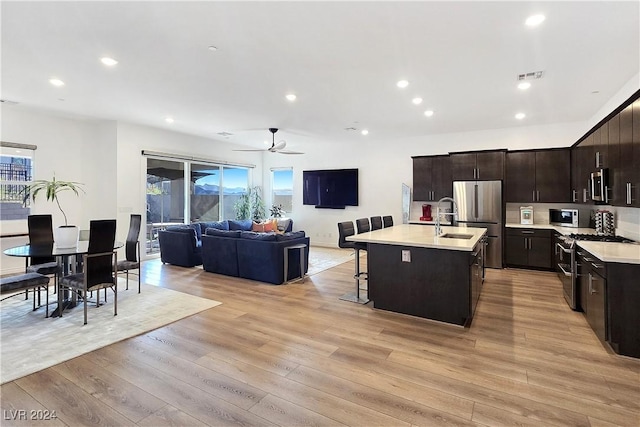 kitchen with an island with sink, a kitchen bar, light hardwood / wood-style floors, stainless steel appliances, and dark brown cabinets