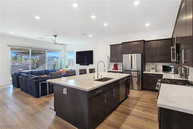 kitchen featuring stainless steel appliances, a kitchen island with sink, sink, and light wood-type flooring