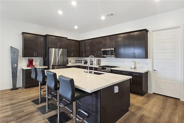 kitchen with a kitchen island with sink, sink, dark brown cabinetry, and appliances with stainless steel finishes