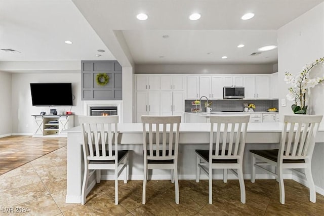 kitchen with sink, decorative backsplash, light wood-type flooring, white cabinetry, and a breakfast bar area