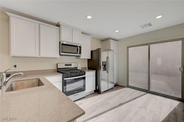 kitchen featuring light stone countertops, stainless steel appliances, sink, light hardwood / wood-style flooring, and white cabinetry