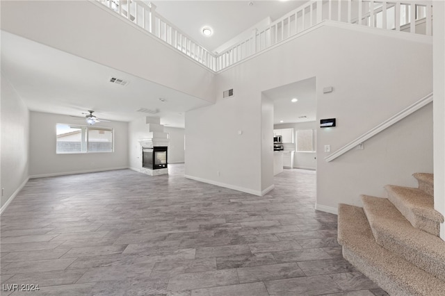 unfurnished living room featuring a multi sided fireplace, ceiling fan, and a towering ceiling