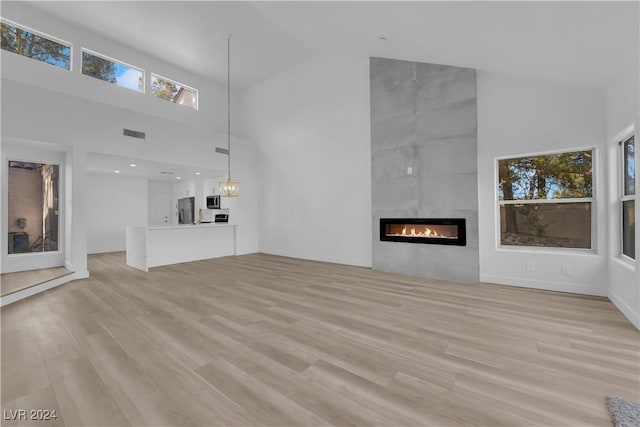 unfurnished living room featuring a fireplace, high vaulted ceiling, and light wood-type flooring