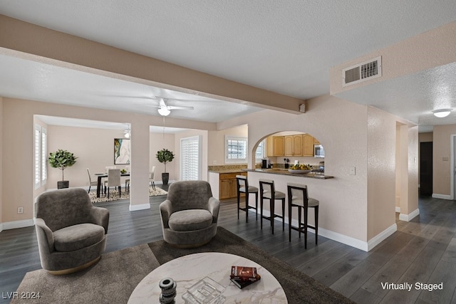 living room with a textured ceiling, ceiling fan, dark wood-type flooring, and beamed ceiling