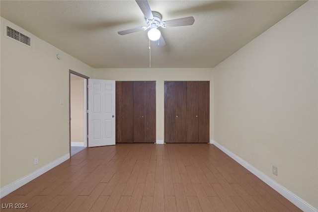 unfurnished bedroom with ceiling fan, two closets, a textured ceiling, and light hardwood / wood-style flooring