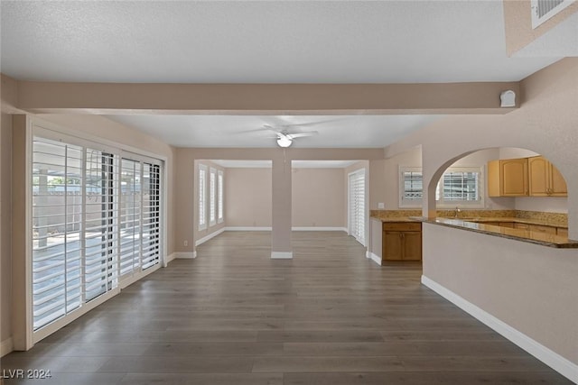 unfurnished living room featuring a textured ceiling, a wealth of natural light, ceiling fan, and dark hardwood / wood-style floors