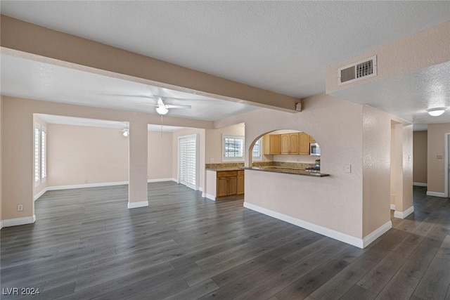 unfurnished living room featuring a textured ceiling, ceiling fan, beam ceiling, and dark wood-type flooring