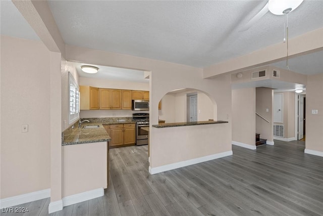 kitchen featuring sink, kitchen peninsula, a textured ceiling, appliances with stainless steel finishes, and light wood-type flooring