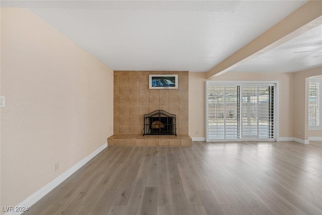 unfurnished living room featuring a tile fireplace, light hardwood / wood-style floors, and beamed ceiling