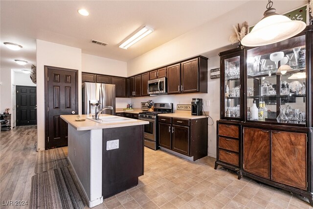 kitchen with sink, stainless steel appliances, decorative light fixtures, a kitchen island with sink, and dark brown cabinets