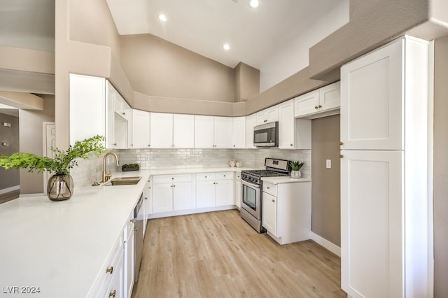 kitchen featuring stainless steel appliances, sink, white cabinets, light hardwood / wood-style floors, and high vaulted ceiling