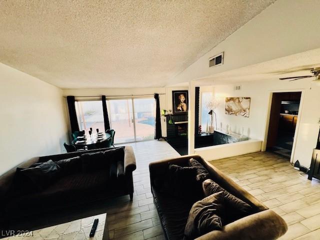 living room with a textured ceiling, ceiling fan, vaulted ceiling, and hardwood / wood-style flooring