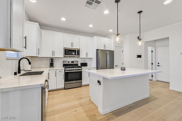 kitchen with appliances with stainless steel finishes, sink, light hardwood / wood-style flooring, a center island, and hanging light fixtures