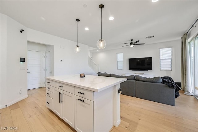 kitchen featuring light stone countertops, pendant lighting, a center island, light hardwood / wood-style floors, and white cabinetry