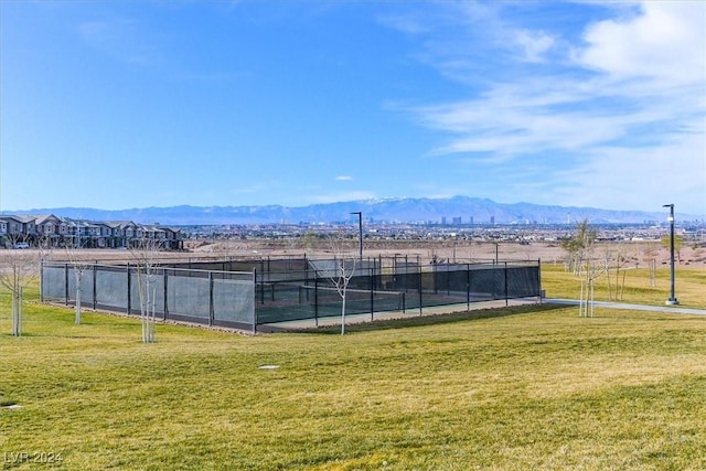 view of tennis court with a lawn, a mountain view, and a rural view