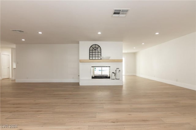 unfurnished living room featuring a multi sided fireplace and light hardwood / wood-style flooring