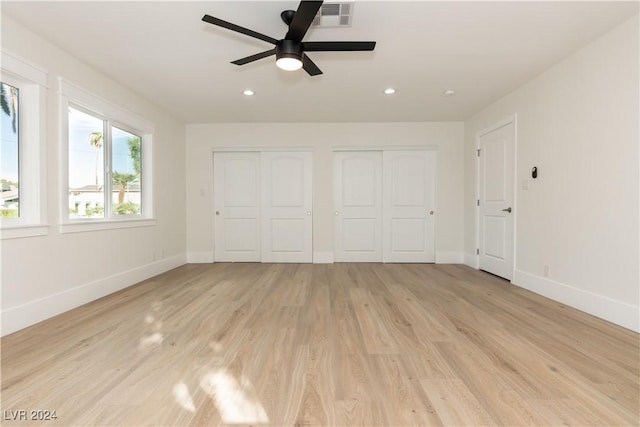 unfurnished bedroom with two closets, light hardwood / wood-style floors, and ceiling fan