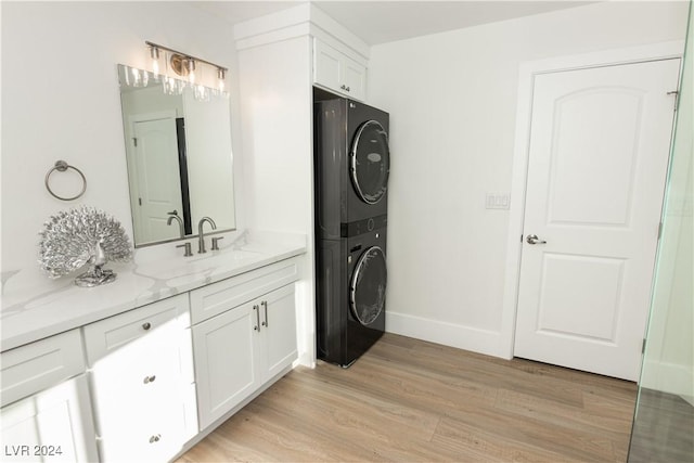 laundry area with stacked washer / drying machine, light hardwood / wood-style floors, cabinets, and sink