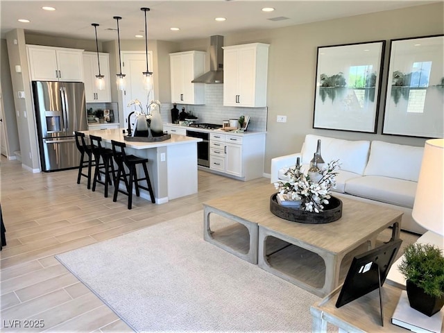 kitchen with white cabinets, wall chimney range hood, hanging light fixtures, decorative backsplash, and stainless steel fridge