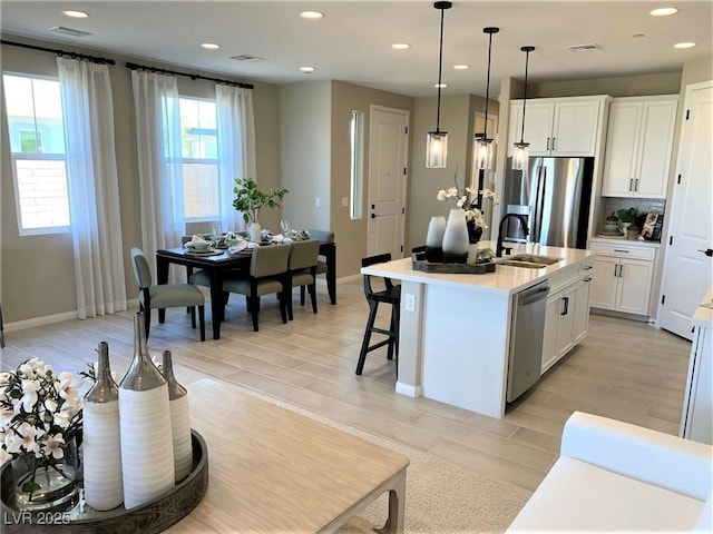 kitchen with white cabinets, decorative light fixtures, an island with sink, and appliances with stainless steel finishes