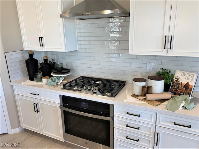 kitchen featuring white cabinets, stainless steel appliances, tasteful backsplash, and wall chimney exhaust hood