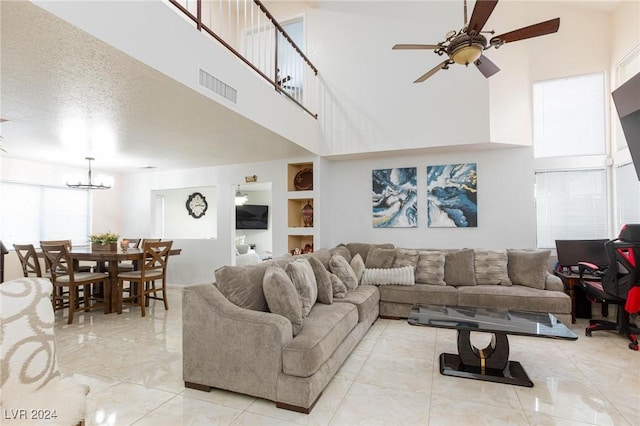 living room with ceiling fan with notable chandelier, built in features, a textured ceiling, and a high ceiling