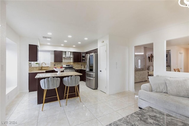 kitchen with backsplash, wall chimney range hood, a kitchen island, dark brown cabinetry, and stainless steel appliances