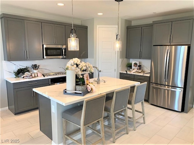 kitchen featuring a kitchen island with sink, gray cabinetry, light stone countertops, and stainless steel appliances