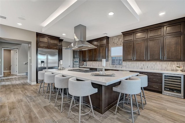 kitchen with island exhaust hood, backsplash, stainless steel appliances, wine cooler, and a large island