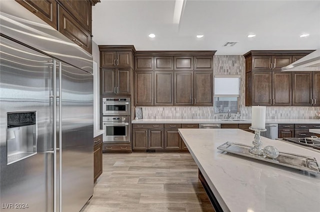 kitchen with dark brown cabinetry, visible vents, light stone countertops, stainless steel appliances, and a sink