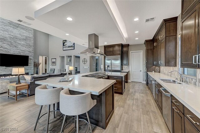 kitchen featuring sink, appliances with stainless steel finishes, range hood, a kitchen island, and a breakfast bar area