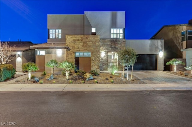 modern home featuring stone siding, driveway, an attached garage, and stucco siding