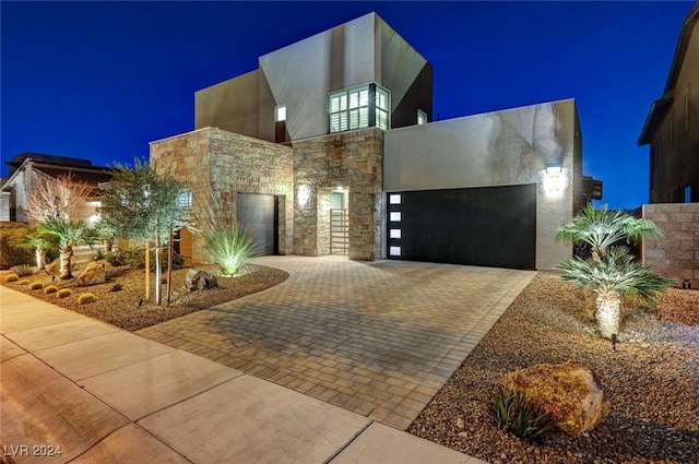 contemporary house featuring decorative driveway, stone siding, an attached garage, and stucco siding