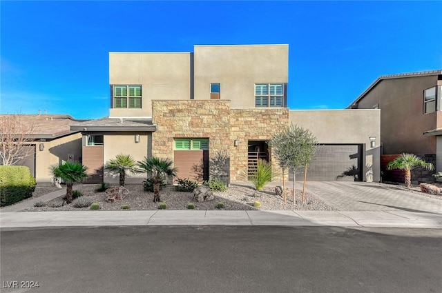 view of front of house featuring a garage, stone siding, decorative driveway, and stucco siding