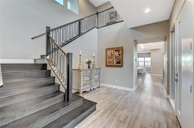 stairs featuring recessed lighting, wood finished floors, a towering ceiling, and baseboards