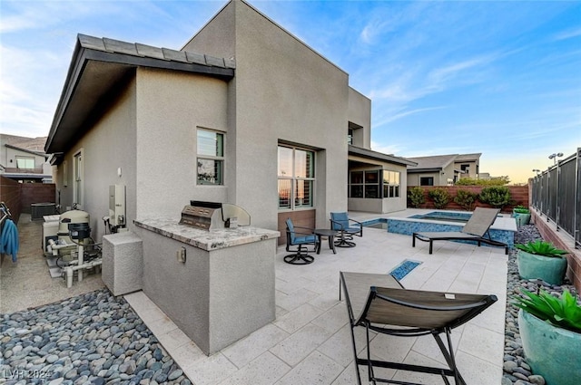 back of house at dusk featuring a hot tub, a patio, exterior kitchen, and a fenced backyard