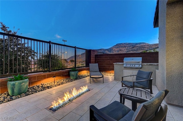 view of patio featuring an outdoor kitchen, a fenced backyard, a mountain view, a fire pit, and grilling area