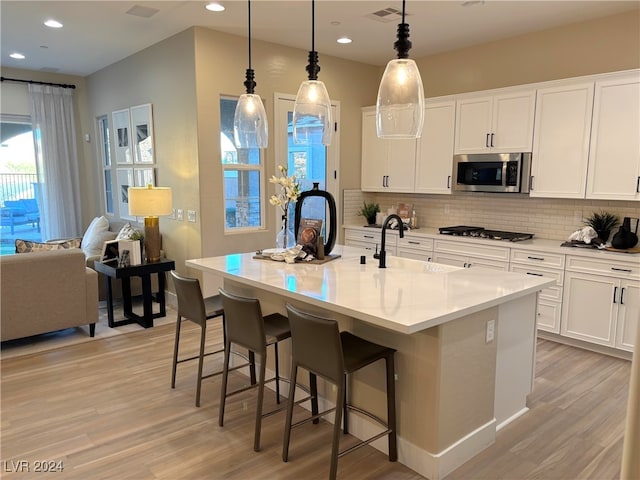 kitchen featuring hanging light fixtures, a center island with sink, white cabinets, and stainless steel appliances